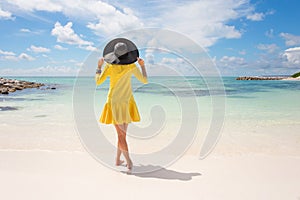 Fashionable woman with black summer hat and yellow dress on the beach