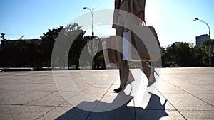 Fashionable woman carries paper packets going along urban street. Young female customer holds shopping bags walks at