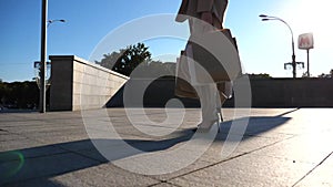 Fashionable woman carries paper packets going along urban street. Young female customer holds shopping bags walks at