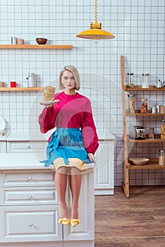fashionable woman in colorful clothes holding plate of pancakes and looking at camera