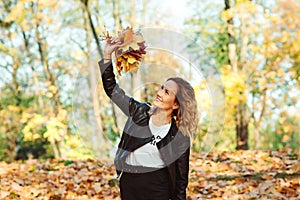 Fashionable woman holding autumn leaves in the park. Stylish girl on a walk in nature
