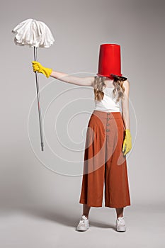 Fashionable woman with a red bucket on her head holding a mop.