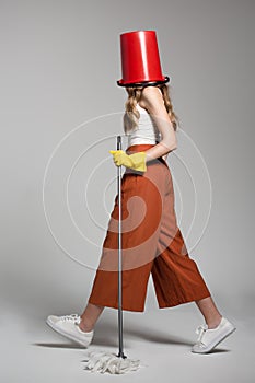 Fashionable woman with a red bucket on her head holding a mop.