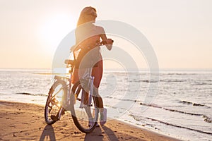 Fashionable woman riding bicycle on the beach at sunset