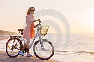 Fashionable woman riding bicycle on the beach at sunset