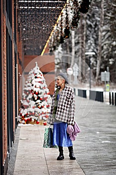 Fashionable woman shopping for Christmas or New Year outside. Model stylish dressed bright colourful dress, tweed jacket