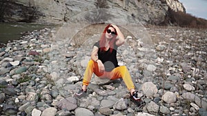 Fashionable woman in sunglasses sitting resting on rocky bank mountain river