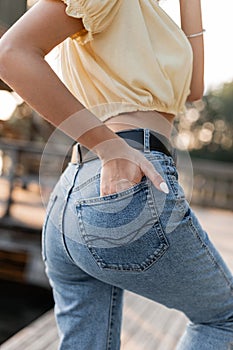 Fashionable woman in trendy blue classic jeans with a beautiful booty walks on the beach, close-up. Woman's hand in back