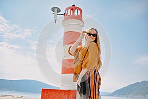 Fashionable woman on vacation against the backdrop of the sea, mountains and a lighthouse. Summer, sunny day, walk along the beach
