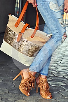 Fashionable woman wearing high heel sandals with fringe, jeans and bag.