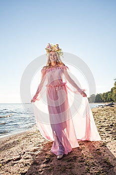 Fashionable woman wearing pink dress and flowers hat on his head on the beach at sunset
