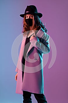 Fashionable woman wearing a protective mask on purple background