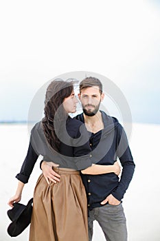 Fashionable woman wearing skirt hugging young man in monophonic winter background.