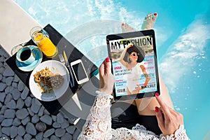 Woman relaxing by the pool and reading emagazine on tablet at breakfast. All contents are made up. photo