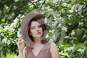 Fashionable young adult woman female model with clean fresh skin, make-up and brown hair in blossom garden on green leaves