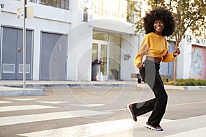Fashionable young African American woman with afro hair running across the street, full length, close up