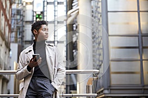 Fashionable young black woman standing in the city holding smartphone, low angle