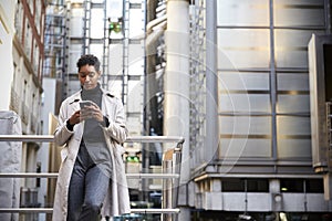 Fashionable young black woman standing in the city leaning on a hand rail using her smartphone, low angle