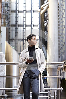 Fashionable young black woman standing in the city leaning on a handrail holding smartphone, low angle, vertical