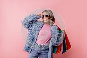Fashionable young blonde caucasian woman with shopping smiles teeth posing on pink background.