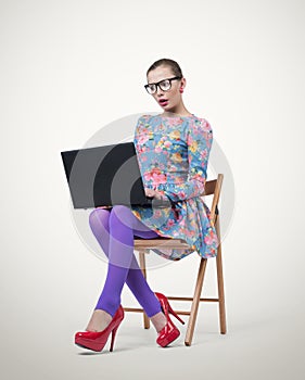 Fashionable young businesswoman in dress and glasses sitting on wooden chair with laptop