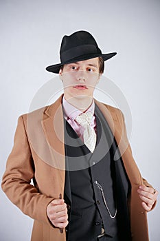 Fashionable young man in black business suit and beige coat with hat on white studio background alone