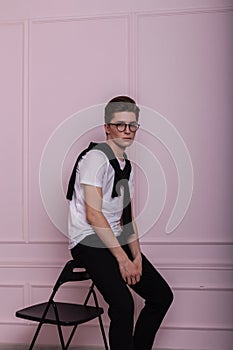 Fashionable young man model in fashion glasses with a hairstyle in a trendy white t-shirt in stylish black jeans sits on a vintage