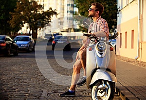 Fashionable young man riding a vintage scooter in street