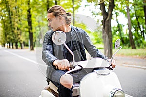 Fashionable young man riding a vintage scooter and looking back in the street