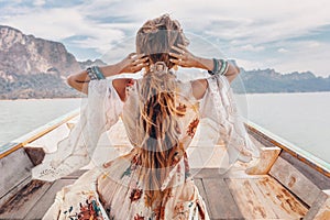 Fashionable young model in boho style dress on boat at the lake