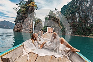 Fashionable young model in boho style dress lying on boat at the lake