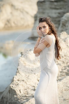 Fashionable young model in a dress stands on a sandy beach