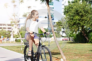 Fashionable young teen girl in shorts and t-shirt rides a bicycle in a summer park