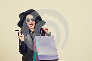 Fashionable young woman in black hat with credit card and colored shopping bags over white studio background.