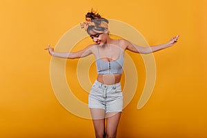 Fashionable young woman in cute tank-top posing on yellow background and waving hands. Smiling enthusiastic girl in good