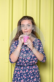 Fashionable young woman drinking juice or smoothie on yellow wall.