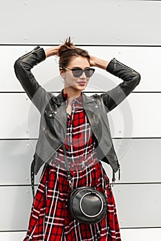 Fashionable young woman hipster with red lips in fashion black-red clothes in sunglasses straightens hairstyle standing on street