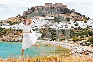 fashionable young woman jumping at the background of white Lindos town in Rhodes. Travel and adventures in Greece
