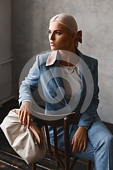 A fashionable young woman with perfect blond hair in an elegant blue suit posing in studio