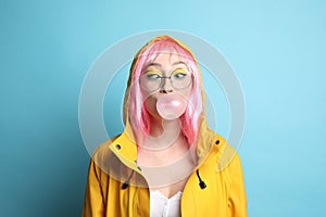 Fashionable young woman in pink wig with bright makeup blowing bubblegum on background