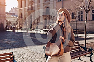 Fashionable young woman posing on street of European city wearing stylish hat and jacket holding handbag. Spring fashion