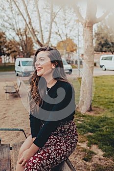 Fashionable young woman sitting on a bench smiling shyly