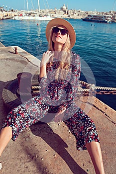 Fashionable young woman sitting and posing at sea dock