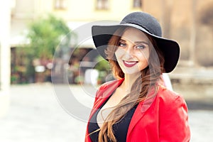 Fashionable young woman is wearing black hat looking at camera outdoors.