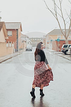 Fashionable young woman wetting her skirt and smiling in the rain with black boots and printed long skirt
