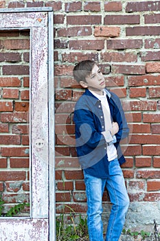 A fashionably dressed guy in a blue shirt stands by an old weathered door against a brick wall