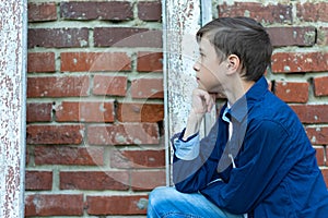 A fashionably dressed guy in a blue shirt stands by an old weathered door against a brick wall