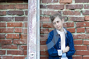 A fashionably dressed guy in a blue shirt stands by an old weathered door against a brick wall. Close-up