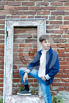 A fashionably dressed guy in a blue shirt stands by an old weathered door against a brick wall. Close-up. Selective focus