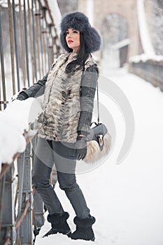 Attractive woman with black fur cap and gray waistcoat enjoying the winter. Side view of fashionable brunette girl posing